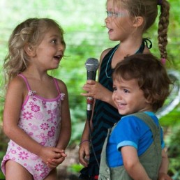 Three children on stage singing and giggling
