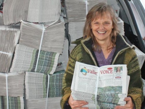 'The Valley Voice' newspaper held up in front of car stacked full of newspapers