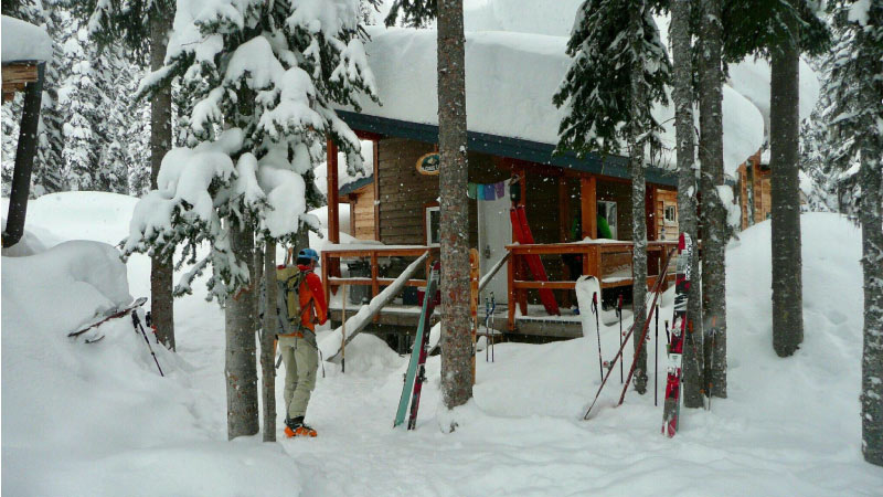 man with skiis outside snowy backcountry lodge